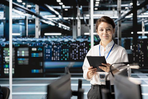 Smiling woman holding a tablet in a modern data center with server racks.