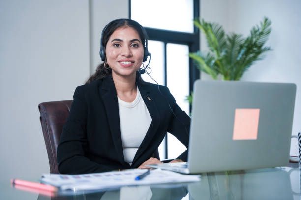 Professional woman in a headset smiling at her desk with a laptop and documents.